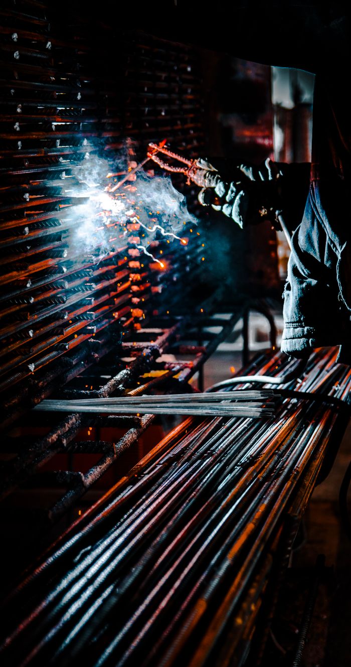 A dramatic vertical shot of a welder at work, producing sparks and smoke in an industrial setting.